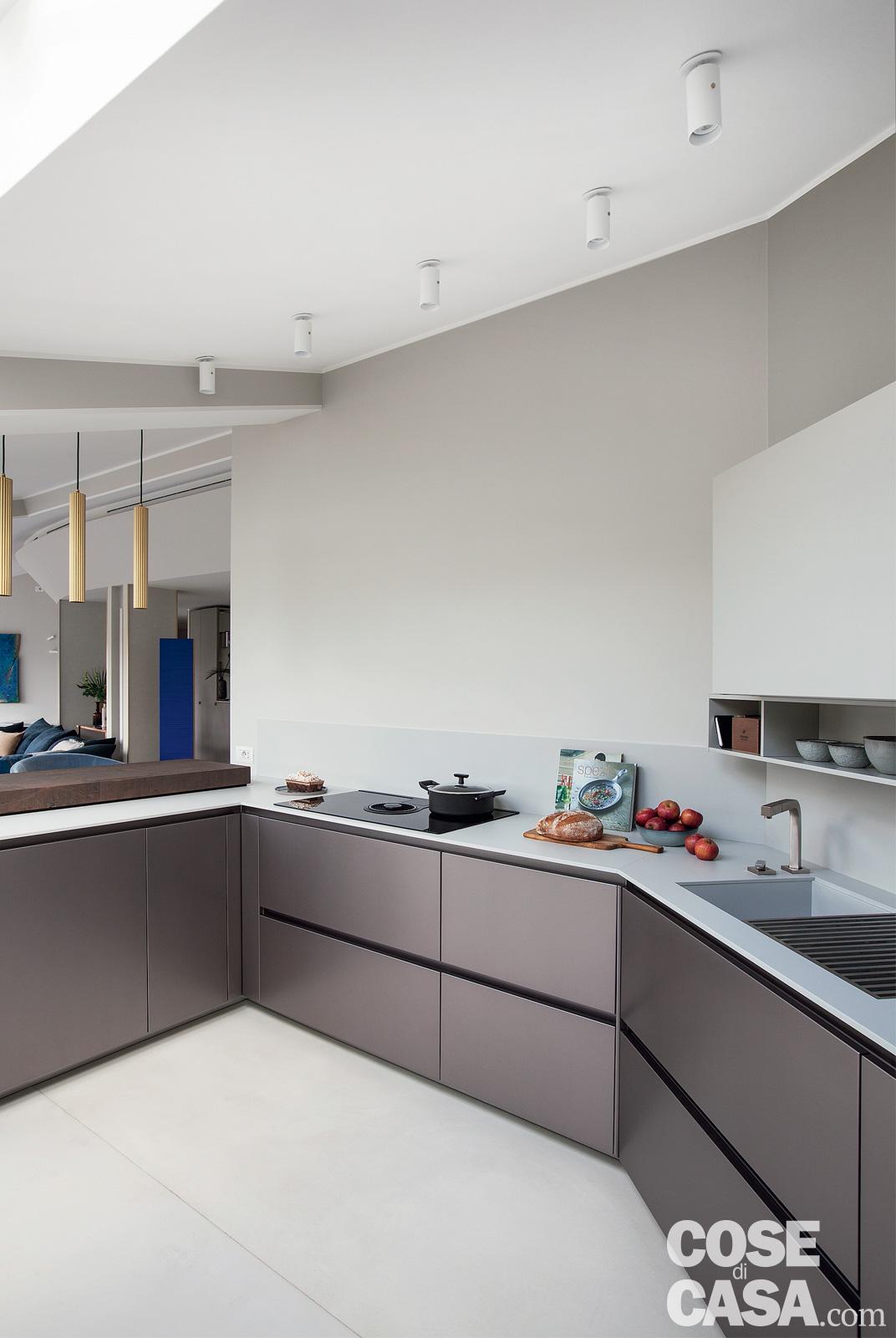 La cucina occupa la zona dell'open space sotto la falda inclinata del tetto, nell'angolo opposto a quello della zona conversazione. L'altezza digradante dello spiovente e i ribassamenti ulteriori dovuti alla presenza delle travi non impediscono comunque di inserire nella composizione anche moduli a colonna e pensili. Le tonalità di grigio dei mobili sono in gradazione con quella del pavimento rivestito in malta. La composizione della cucina, su due lati più l'elemento a penisola che separa la zona operativa dal soggiorno, fa parte del programma One 80 di Ernestomeda nei colori Titanium e grigio rugiada. Il top e il lavello integrato sono in Stone+, il rubinetto è Su & Giù di Gessi. Il piano cottura a induzione con cappa aspirante integrata è di AEG. La cucina occupa la zona dell'open space sotto la falda inclinata del tetto, nell'angolo opposto a quello della zona conversazione. L'altezza digradante dello spiovente e i ribassamenti ulteriori dovuti alla presenza delle travi non impediscono comunque di inserire nella composizione anche moduli a colonna e pensili. Le tonalità di grigio dei mobili sono in gradazione con quella del pavimento rivestito in malta. La composizione della cucina, su due lati più l'elemento a penisola che separa la zona operativa dal soggiorno, fa parte del programma One 80 di Ernestomeda nei colori Titanium e grigio rugiada. Il top e il lavello integrato sono in Stone+, il rubinetto è Su & Giù di Gessi. Il piano cottura a induzione con cappa aspirante integrata è di AEG.