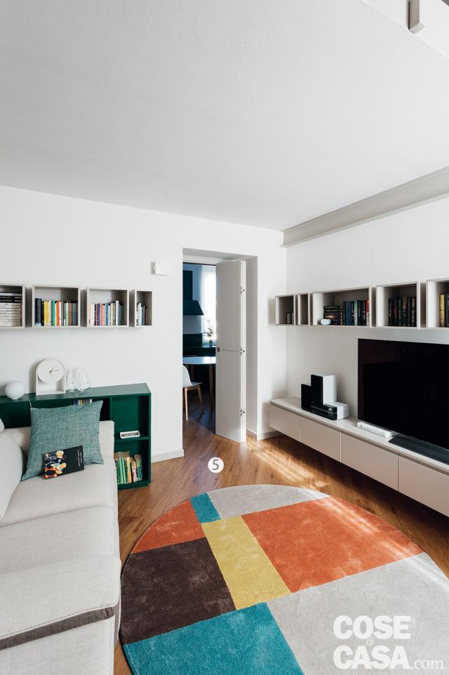 soggiorno del sottotetto green, zona conversazione, divano bianco, mobile tv sospeso, pensili a giorno, tappeto a motivi geometrici, pavimento in parquet, porta a libro soggiorno del sottotetto green, zona conversazione, divano bianco, mobile tv sospeso, pensili a giorno, tappeto a motivi geometrici, pavimento in parquet, porta a libro