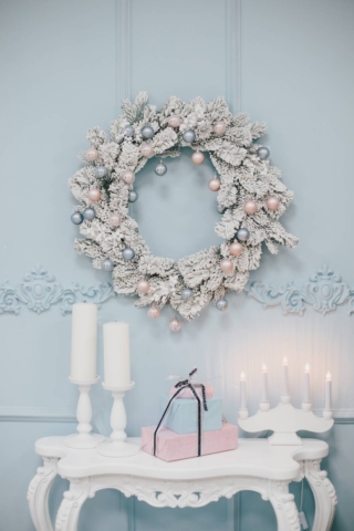 Christmas interior: hand made wreath on the blue wall, candles and boxes with presents on white vintage table. Christmas interior: hand made wreath on the blue wall, candles and boxes with presents on white vintage table.
