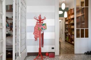 3. A righe
Un grande atrio quadrato, tipico delle case d’epoca, che conduce allo studio, al salotto e al corridoio che porta alla zona notte attraverso grandi vetrate. Lo stile è classico, con il pavimento in marmo bianco e grigio. Ma l’insieme un po’ austero è stato smitizzato grazie alla scelta di dipingere le pareti a fasce orizzontali, con righe alte circa 40 centimetri, che alternano il grigio chiaro e il bianco. Sempre con l’ottica di rendere l’ingresso più friendly il vecchio appendiabiti da terra è stato dipinto a  smalto rosso, mentre sullo sfondo si intravvedono tre lampade di carta di forme diverse montate su cavi rossi con altezze alternate.