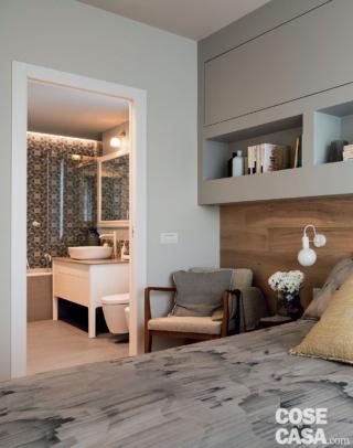 Nella camera matrimoniale, ai due lati del giroletto tessile, i tavolini a tre gambe con piano sagomato sono di Dialma Brown, così come la poltroncina a sinistra con struttura in legno. Le applique con diffusore sferico fissate alla boiserie sono di Vesoi.