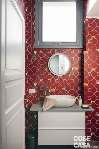 bagno del mini appartamento, carta da parati coor mattone con i tucani, mobile sospeso, lavabo da appoggio, finestra, secchio rotondo, porta bugnata in laccato bianco bagno del mini appartamento, carta da parati coor mattone con i tucani, mobile sospeso, lavabo da appoggio, finestra, secchio rotondo, porta bugnata in laccato bianco