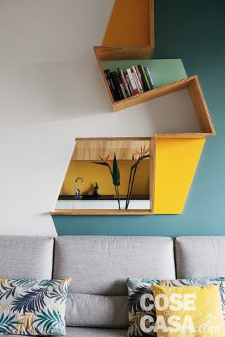 soggiorno, libreria a zig zag in legno, divano grigio, cuscini, finestra interna tra la zona conversazione e la cucina soggiorno, libreria a zig zag in legno, divano grigio, cuscini, finestra interna tra la zona conversazione e la cucina