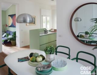 soggiorno, zona pranzo, tavolo con piano bianco, specchio tondo, penisola della cucina in finitura verde acqua, sospensione cromata, sedie verdi soggiorno, zona pranzo, tavolo con piano bianco, specchio tondo, penisola della cucina in finitura verde acqua, sospensione cromata, sedie verdi