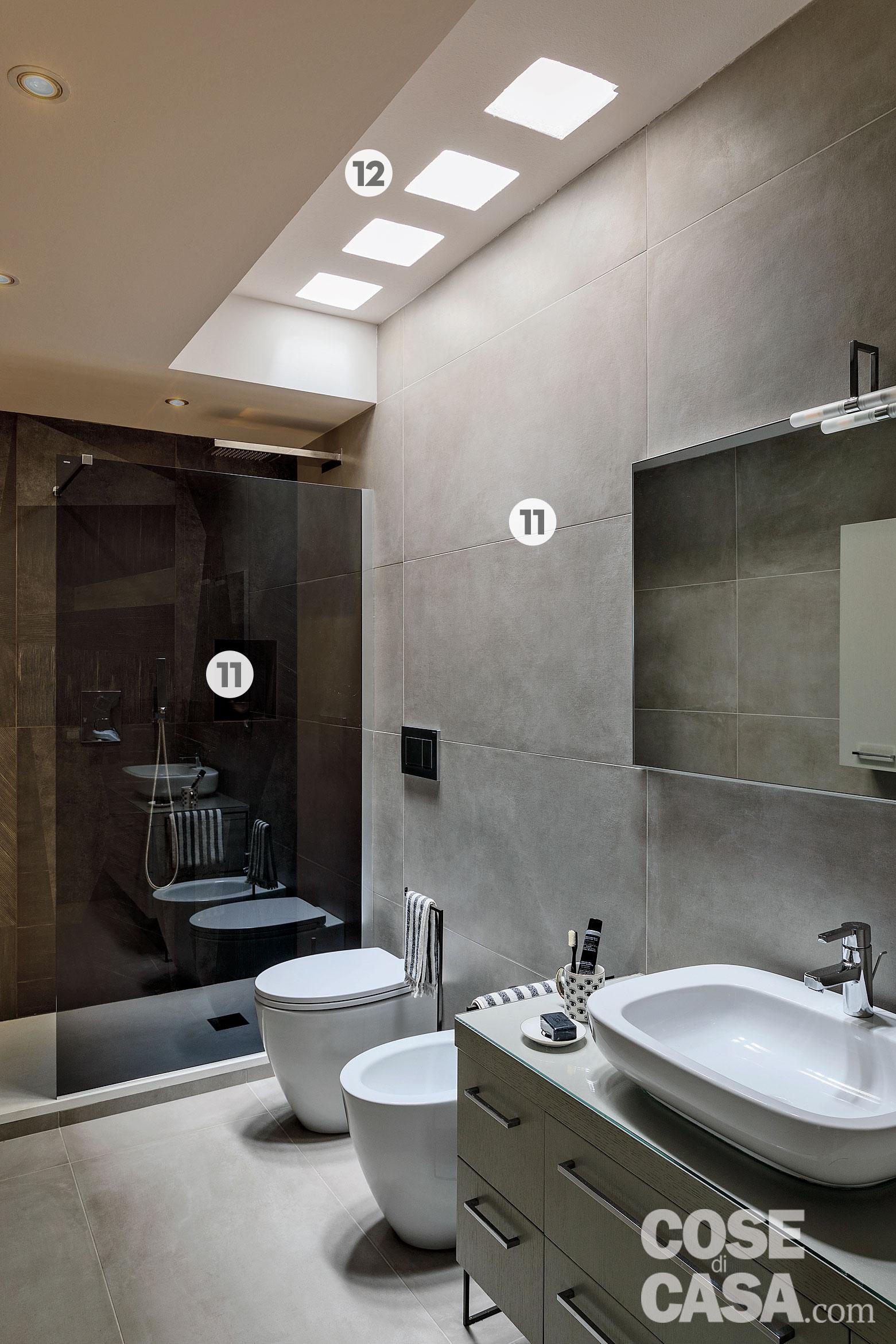 Nel bagno di forma lunga e stretta, il grigio uniforma le finiture delle pareti, con l'eccezione di quelle della doccia: il rivestimento, qui molto scuro, ne fa quasi scomparire il volume, appiattendone la profondità. A soffitto, intorno al lucernario, il ribassamento in cartongesso di elevato spessore ha soprattutto lo scopo di nascondere la trave strutturale che attraversa la stanza. Nel bagno i rivestimenti a parete e a terra effetto cemento sono in gres porcellanato della serie One di Ceramiche Caesar; le piastrelle scure all'interno della doccia sono invece della coll. La Palladiana di Bardelli. Il mobile lavabo è di Idea Group, la rubinetteria di Grohe; sanitari della coll. Velis di Catalano. Le spugne sono di Fazzini, gli accessori di Coin casa. Nel bagno di forma lunga e stretta, il grigio uniforma le finiture delle pareti, con l'eccezione di quelle della doccia: il rivestimento, qui molto scuro, ne fa quasi scomparire il volume, appiattendone la profondità. A soffitto, intorno al lucernario, il ribassamento in cartongesso di elevato spessore ha soprattutto lo scopo di nascondere la trave strutturale che attraversa la stanza. Nel bagno i rivestimenti a parete e a terra effetto cemento sono in gres porcellanato della serie One di Ceramiche Caesar; le piastrelle scure all'interno della doccia sono invece della coll. La Palladiana di Bardelli. Il mobile lavabo è di Idea Group, la rubinetteria di Grohe; sanitari della coll. Velis di Catalano. Le spugne sono di Fazzini, gli accessori di Coin casa.