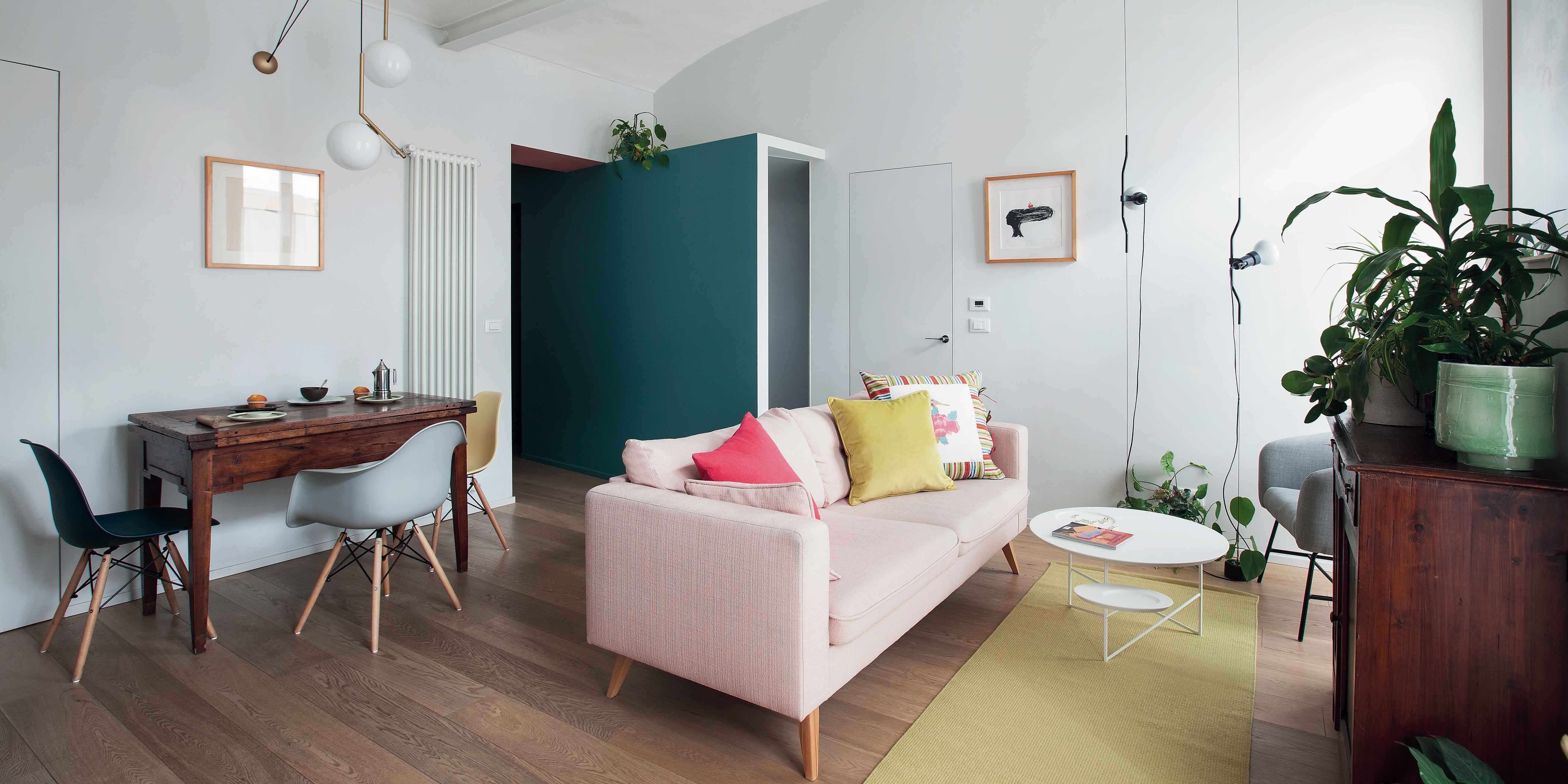 zona giorno del trilocale, divano rosa, cuscini gialli e rossi, tavolino bianco rotondo, sospensioni di design, passatoria gialla, pavimento in parquet, mobili di famiglia, sedute di design anni '50, radiatore verticale, parete color ottanio