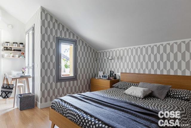 Vista della camera da letto matrimoniale che, oltre agli spazi di contenimento collocati nel punto più basso dell'ambiente (sulla destra rispetto a questa foto, sono visibili in pianta), può usufruire di un'area studio. Le tonalità calde del rovere e il decoro geometrico alle pareti danno all'ambiente una forte caratterizzazione stilistica. Vista della camera da letto matrimoniale che, oltre agli spazi di contenimento collocati nel punto più basso dell'ambiente (sulla destra rispetto a questa foto, sono visibili in pianta), può usufruire di un'area studio. Le tonalità calde del rovere e il decoro geometrico alle pareti danno all'ambiente una forte caratterizzazione stilistica.