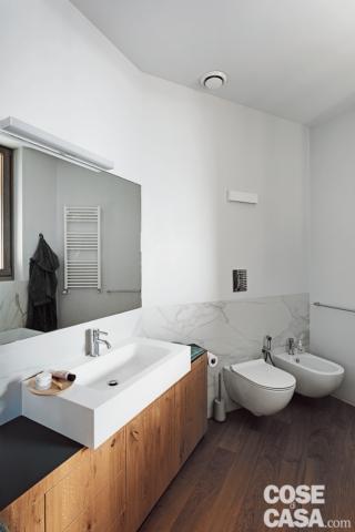 bagno del nuovo appartamento, mobile con frontali in legno, piano nero, lavabo a semincasso, specchiera, applique, sanitari sospesi, rivestimento in marmo bianco a parete, pavimento in parquet, scaldasalviette bianco bagno del nuovo appartamento, mobile con frontali in legno, piano nero, lavabo a semincasso, specchiera, applique, sanitari sospesi, rivestimento in marmo bianco a parete, pavimento in parquet, scaldasalviette bianco