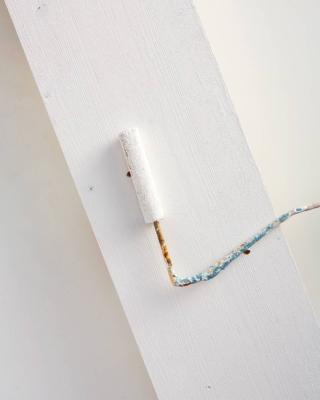 Dopo aver eseguito i fori, carteggiare i bordi con una cartavetrata a grana fine; poi, con un panno, eliminare la polvere ed eventuali schegge. Pitturare l’asse con una mano di primer aggrappante, lasciando asciugare e ripetendo l’operazione sul retro e sui bordi.
Per facilitare l'operazione, utilizzare un rullo per pittura e un pennello a punta tonda, così da stendere il colore anche sugli spessori.