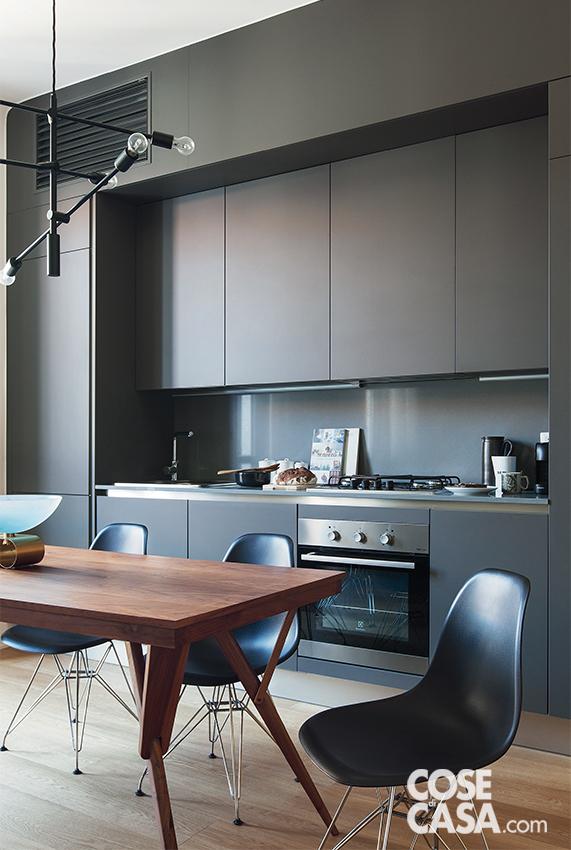 Nella zona cottura la composizione in linea con basi, pensili e due colonne laterali in finitura antracite opaco e alzata in laccato lucido è di Veneta Cucine. Il piano cottura a gas e il forno multifunzione con estetica inox sono di Electrolux. In alto, il tamponamento in cartongesso tinteggiato nella stessa tonalità antracite dei mobili, nasconde uno degli split dell'impianto di climatizzazione e integra la griglia per la diffusione dell'aria fresca.