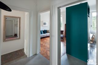 corridoio, vani d'accesso al soggiorno e alla cucina, colonna frigo, pavimento in rena cementizia, parquet a spina di pesce, specchio vintage, porte in legno laccato bianco e vetro