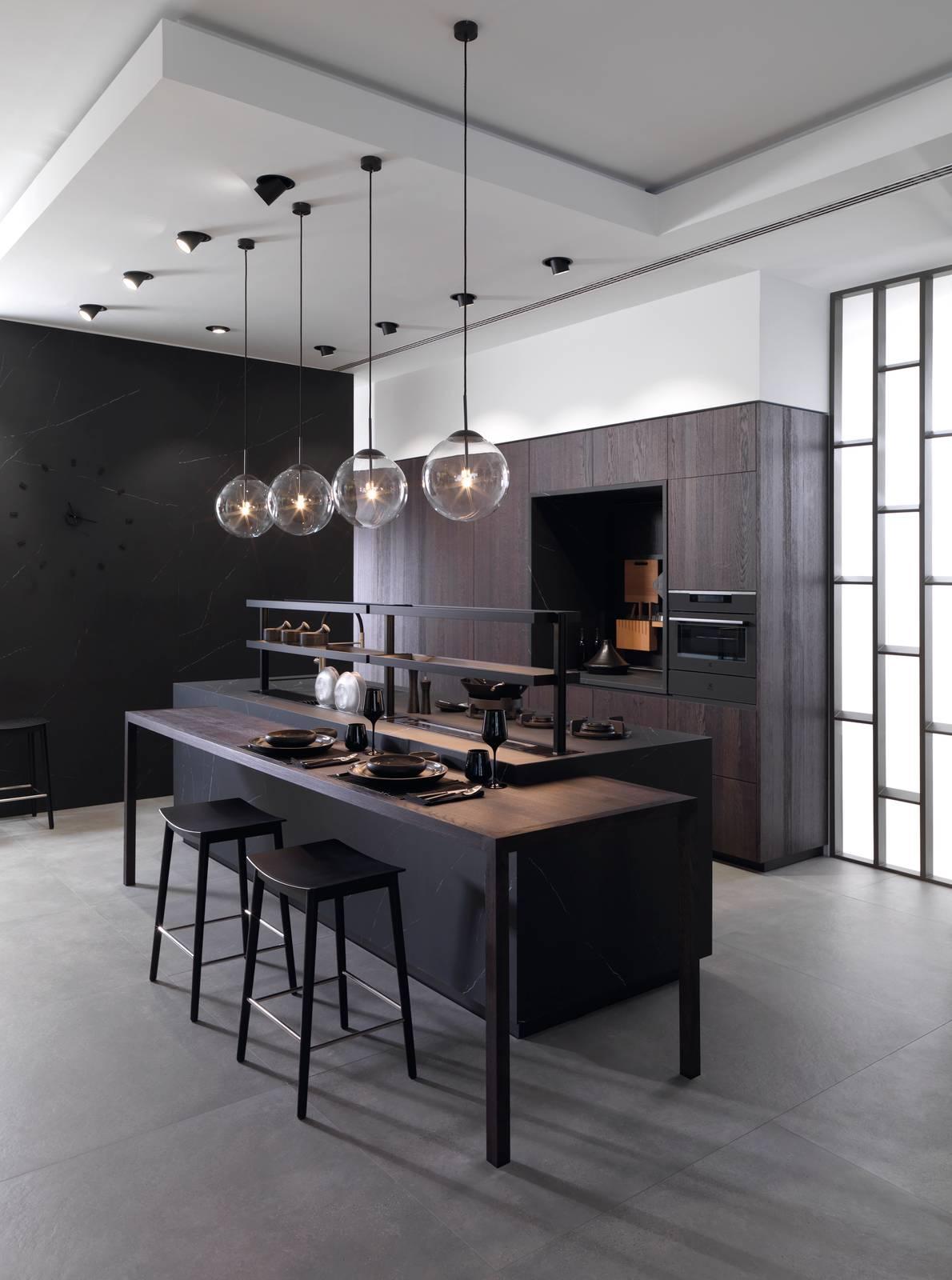 Eleganti tonalità scure per la composizione E9.30 di Gamadecor che alterna le ante realizzate in Xtone Liem Black Nature a quelle impiallacciate in legno spazzolato Roble Noche. L'assenza di maniglie sulla superficie della ante permette di godere appieno della venatura del legno e del disegno effetto marmo. L'isola, dalla dimensioni imponenti, è dotata di un lungo piano snack, di un'alzatina e del sistema VES costituito da un vano incassato nel top in cui sono inseriti scomparti per gli utensili da cucina. Prezzo su richiesta. www.gama-decor.com Eleganti tonalità scure per la composizione E9.30 di Gamadecor che alterna le ante realizzate in Xtone Liem Black Nature a quelle impiallacciate in legno spazzolato Roble Noche. L'assenza di maniglie sulla superficie della ante permette di godere appieno della venatura del legno e del disegno effetto marmo. L'isola, dalla dimensioni imponenti, è dotata di un lungo piano snack, di un'alzatina e del sistema VES costituito da un vano incassato nel top in cui sono inseriti scomparti per gli utensili da cucina. Prezzo su richiesta. www.gama-decor.com