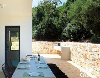 cucina della casa di vacanze, finestra, piano cottura a gas, tendaggi, portafinestra, tavolo rettangolare, sedie, panchetta, sospensioni con diffusore verde, quadri a parete, faretti, pavimento in resina