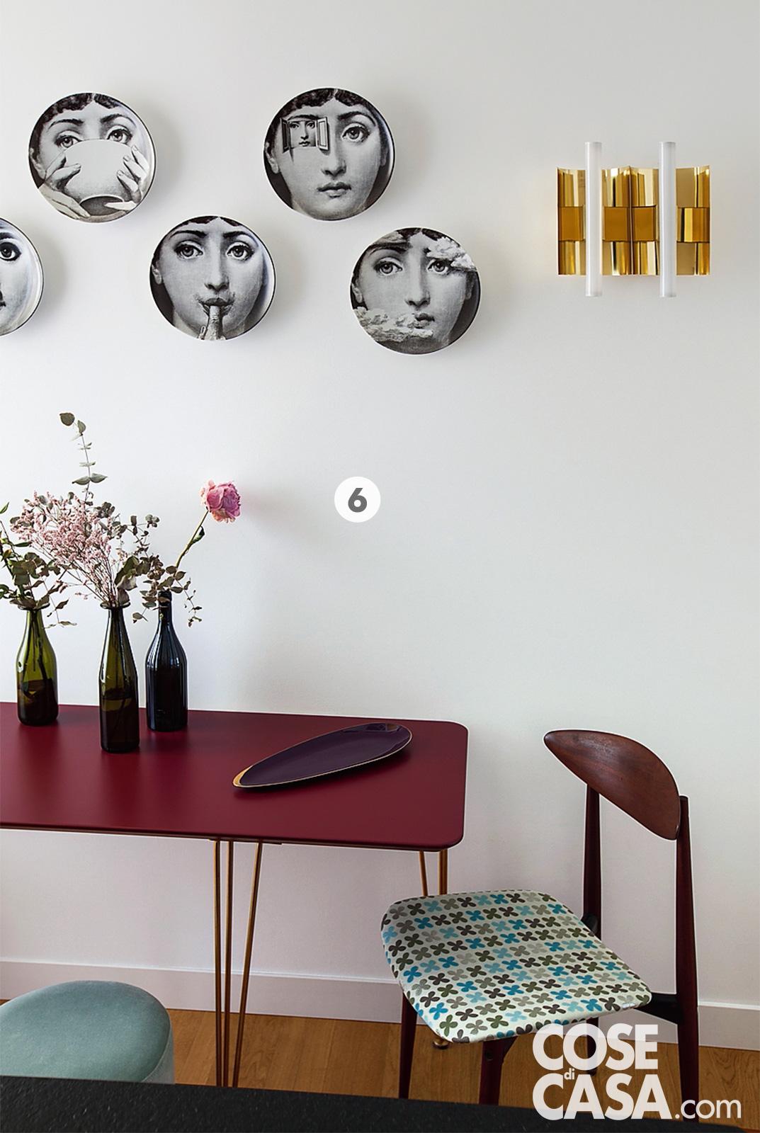 Il tavolo della cucina ha il piano in mdf color amaranto, sulla parete piatti decorativi di Fornasetti Il tavolo della cucina ha il piano in mdf color amaranto, sulla parete piatti decorativi di Fornasetti