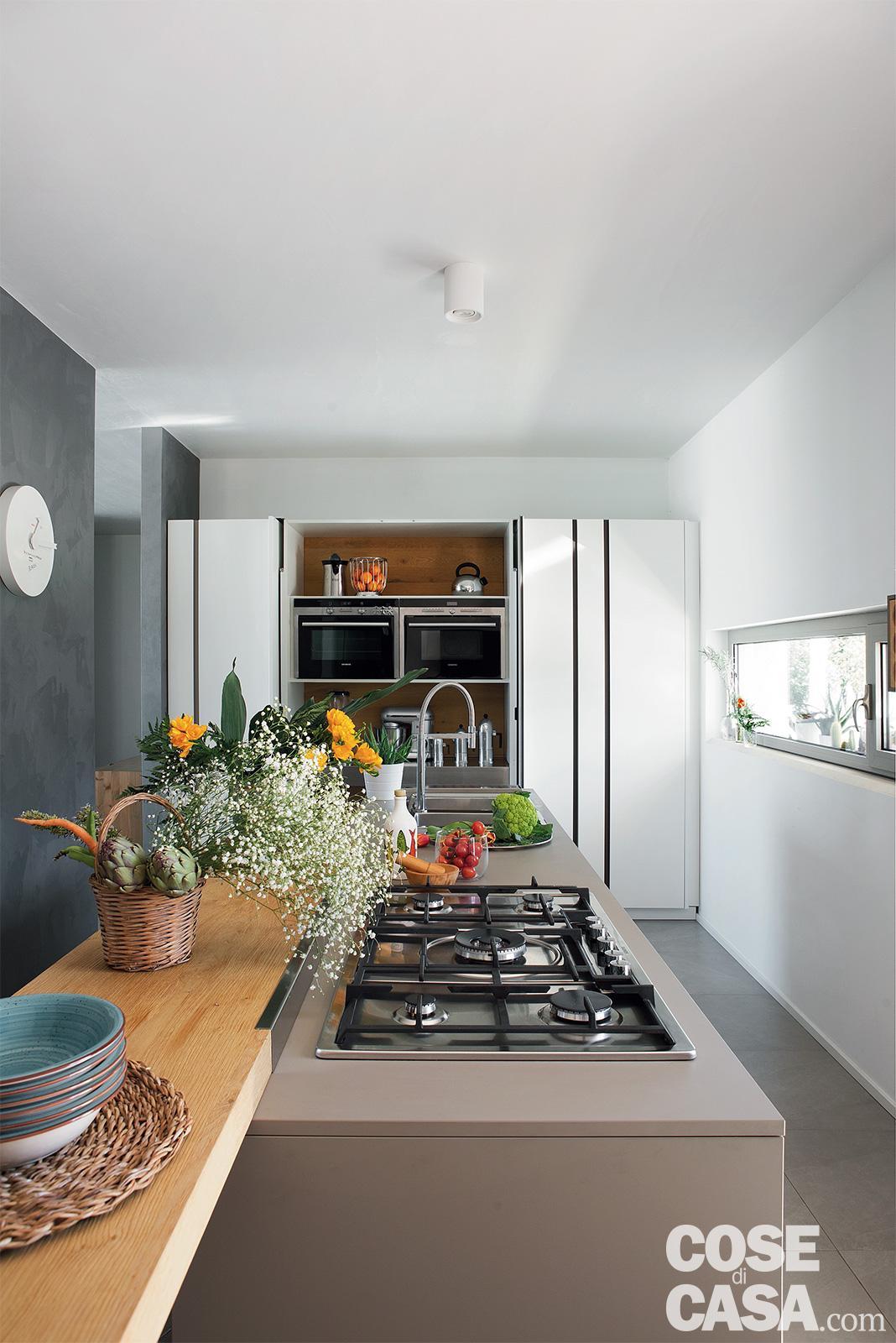 Una cucina con una grande isola con sgabelli neri e piano di lavoro bianco  con piano di lavoro nero.