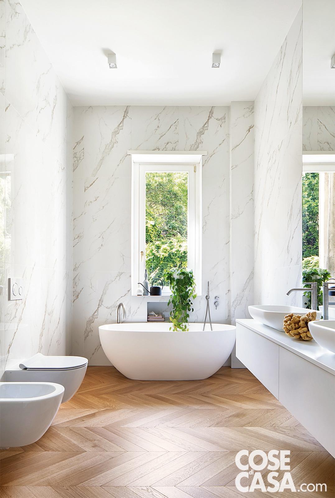 bagno con vasca freestanding, pareti marmo carrara e pavimento in parquet a spina di pesce