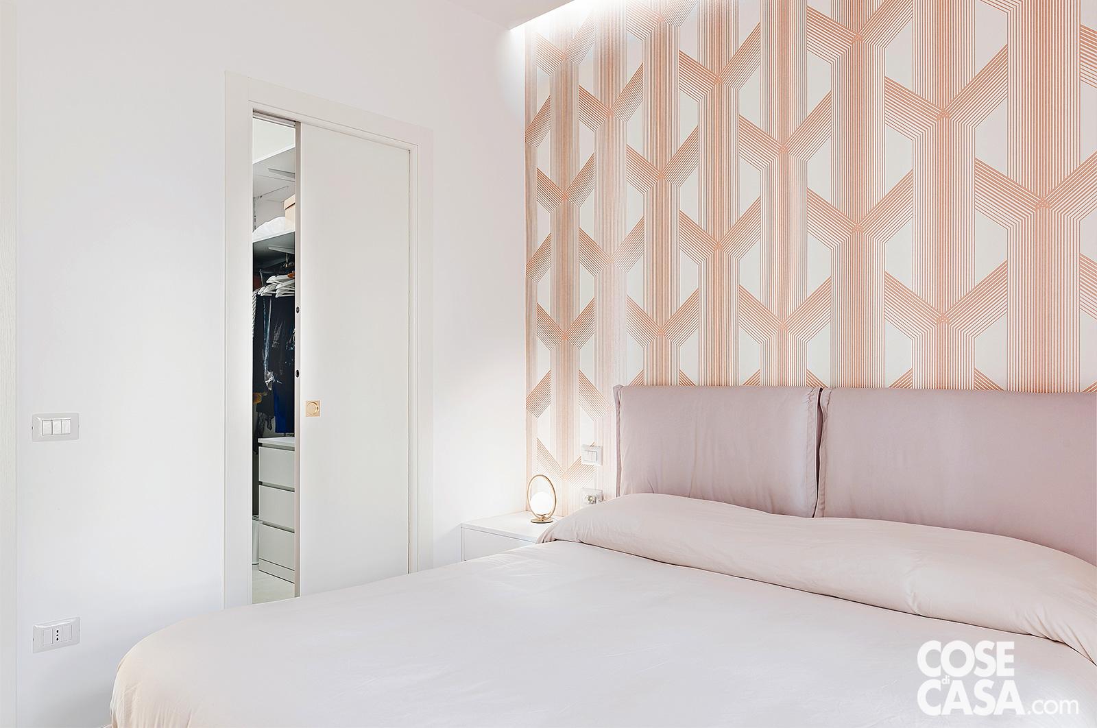 Camera da letto con testiera imbottita e parete decorata con motivi geometrici, porta scorrevole aperta che mostra la cabina armadio.
