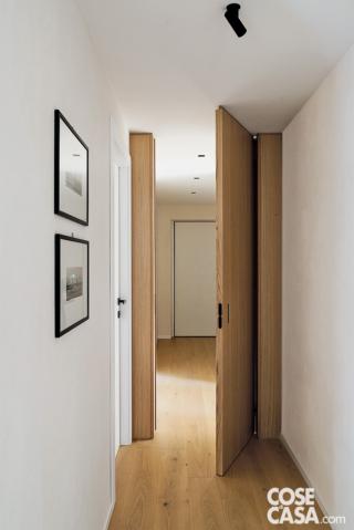corridoio, porta in legno rasomuro, stampe incorniciate a parete, faretto nero orientabile a soffitto, pavimento in parquet