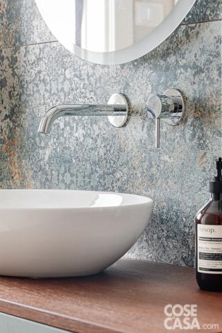 Dettaglio del lavabo in ceramica bianca con rubinetto cromato su parete decorata con piastrelle effetto pietra