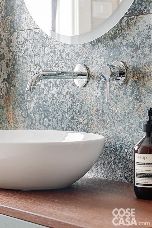 Dettaglio del lavabo in ceramica bianca con rubinetto cromato su parete decorata con piastrelle effetto pietra