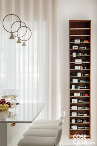 Porta-bottiglie verticale in legno con diverse bottiglie di vino, posizionato accanto alla cucina in uno spazio luminoso