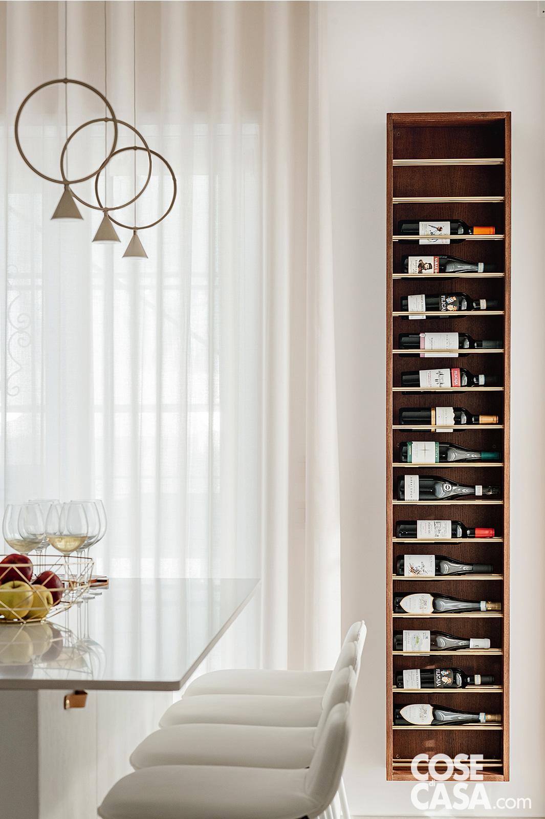 Porta-bottiglie verticale in legno con diverse bottiglie di vino, posizionato accanto alla cucina in uno spazio luminoso