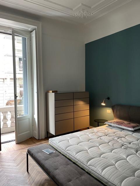 Sono arrivati i mobili e montate le luci, con la calotta dorata orientabile per poter leggere quando si è a letto.  In fondo al letto, caratterizzato da una testata avvolgente, c’è una panchetta coordinata: un dettaglio che quando c’è spazio davanti al letto aggiunge un tocco in più alla camera. A lato c’è un piccolo comodino tondo e una cassettiera laccata color tortora, comodissima per la biancheria. Tutti i mobili sono Di Molteni, mentre le luci sono di Tooy