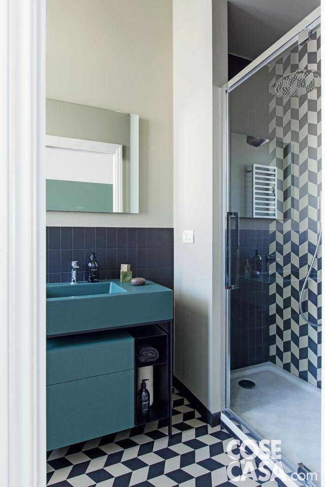 Pavimento e doccia sono rivestiti con piastrelle a losanghe bianche e blu che creano un disegno dinamico. Il resto delle pareti è chiaro oppure - dietro al mobile lavabo  verde petrolio -rivestito in piastrelle blu rettangolari, posate in verticale. Pavimento e doccia sono rivestiti con piastrelle a losanghe bianche e blu che creano un disegno dinamico. Il resto delle pareti è chiaro oppure - dietro al mobile lavabo  verde petrolio -rivestito in piastrelle blu rettangolari, posate in verticale.