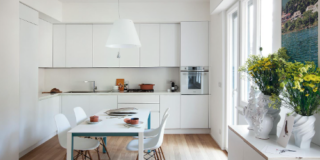 Cucina bianca e luminosa con finestre senza tende totalmente aperta sul living.