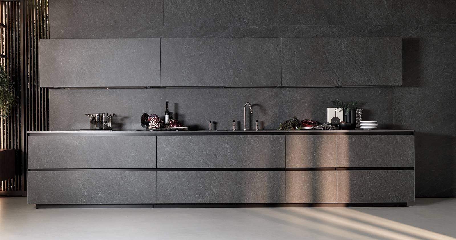 Si sviluppa linearmente lungo la parete la composizione Telero di Euromobil che è composta da basi e pensili con le ante in gres Laminam In-Side Cardoso nero con un aspetto piacevolmente materico; il profilo gola è realizzato in alluminio anodizzato nero spazzolato. Il piano e gli schienali  coordinati nella finitura rendono la composizione armoniosa e uniforme sottolineandone la colorazione scura. Prezzo su richiesta. www.euromobil.com