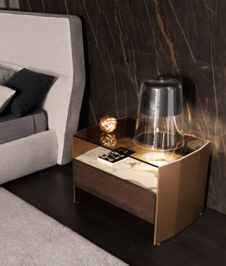 Il comodino Milvian di MisuraEmme, designer Francesco Lucchese, è dotato di un ripiano in vetro trasparente e di un cassetto con finitura interna in nobilitato Primo Fiore, montati su spalle sagomate in alluminio verniciato Bronzo. Il fronte del cassetto è realizzato in essenza lucida o opaca; il ripiano è in pregiato marmo bianco con venatura in contrasto. È disponibile in due formati. Misura L 71 x P 51,4 x H 48,5 cm. Prezzo su richiesta. https://www.misuraemme.it