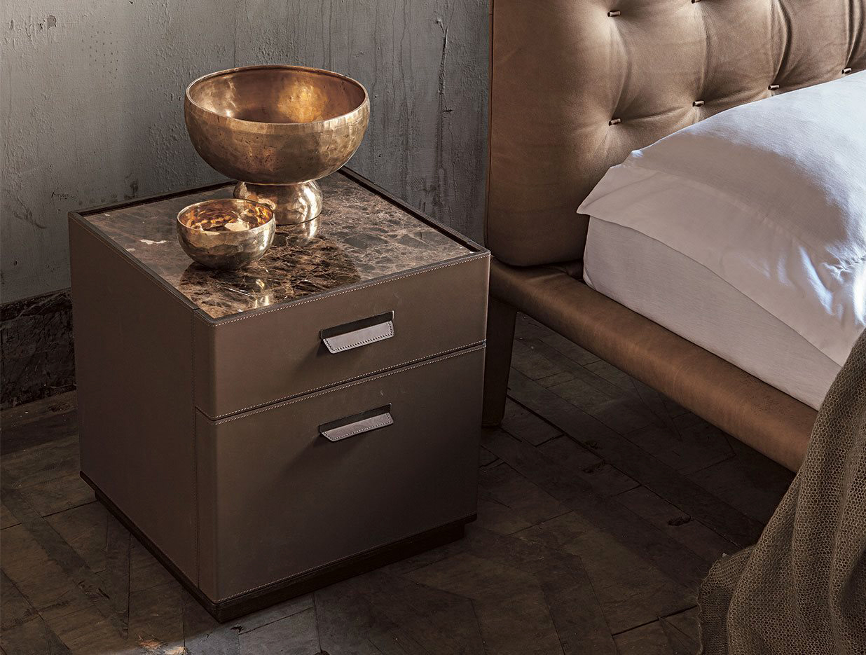 Un pregiato rivestimento in cuoio con cucitura decorativa per il comodino Skin di Alivar, designer Giuseppe Bavuso, che ha la struttura realizzata in rovere termotrattato o in noce nazionale. I due cassetti sono dotati di maniglie in metallo rivestite in cuoio e di guide metalliche frenanti. Il piano è disponibile in marmo o in cuoio. Misura L 45 x P 43 x H 48 cm. Prezzo su richiesta. https://www.alivar.it