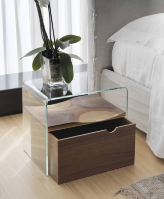 Il comodino Bifronte di Horm, designer Toyo Ito, è composto da un ponte in vetro extra chiaro curvato, da un ripiano in legno massello multistrato in cinque differenti legni (noce canaletto, mogano, ciliegio, rovere e frassino) e da un cassetto scorrevole su ruote in MDF impiallacciato in noce canaletto con il fronte noce canaletto. Misura L 52 x P 37 x H 46 cm. Prezzo 864 euro. https://www.horm.it