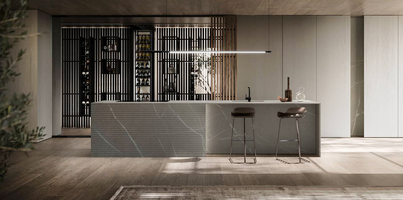 Fa parte del nuovo programma Blade Lab di Modulnova la cucina dominata dalla presenza dell'imponente isola e della grande cantina vini. L'isola è in pietra Piasentina fiammata con una lavorazione millerighe che dona dinamicità alla pietra; le colonne terra soffitto in Laccato Metal Ivory  delineano l'ambiente. La cantina è protetta da una vetrata grigio fumé con anta a bilico e, al suo interno, si trova il sistema interparete Solid retroilluminato costituito da listelli verticali in legno di Noce grigio, arricchito da una boiserie e da elementi a giorno che possono essere posizionati a piacere; è completata da una vetrina vini refrigerante e personalizzabile nella dimensione, nella profondità e nello schienale. https://www.modulnova.it - Fuorisalone, Modulnova Milano– Corso Garibaldi 99, Milano