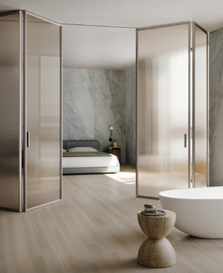 La porta interna L7 Bi-folding di Lualdi con le ante a libro nella raffinata texture Mini Flutes, realizzata in vetro cannettato, nella variante di colore bronzo satinato, permette di definire l'intimità e i diversi spazi del vivere, dalla casa all'ufficio passando per l' hotellerie; i profili e le maniglie in alluminio nella versione Titanium, che aggiunge un tocco di eleganza e calore, senza compromettere la leggerezza complessiva. https://www.lualdi.com - Salone del Mobile, padiglione 9, stand H11.