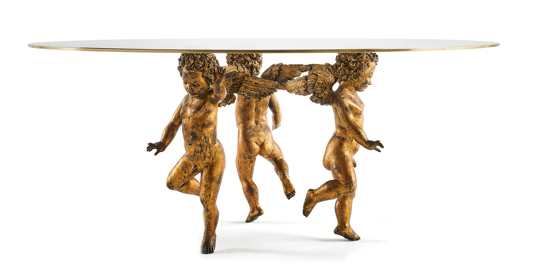 Una base scultorea, composta da tre amorini in fusione di ottone con finitura foglia oro anticata patinata, per il tavolino Anges di Jumbo Collection; il piano rotondo in cristallo extra chiaro con bisello in foglia oro permette di godere appieno della scenografica base di ispirazione barocca. Misura Ø 140 x H 62 cm. https://jumbocollection.com - Salone del Mobile, padiglione 13, stand L11-M14.