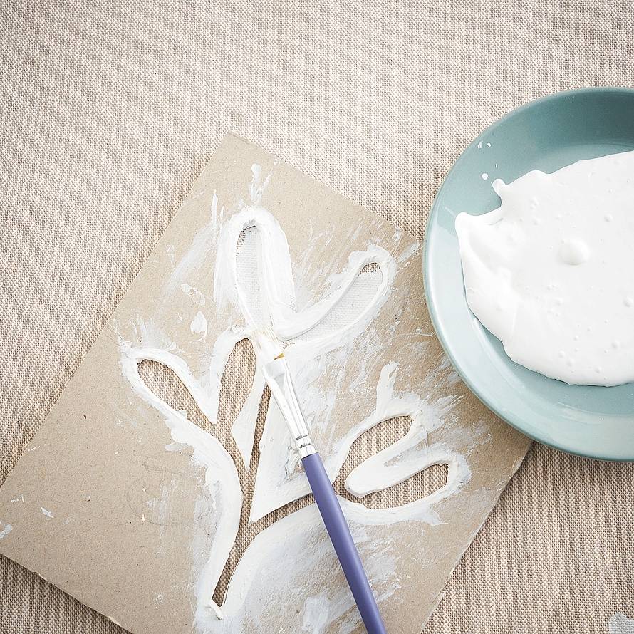 Appoggiare la tovaglia su una superficie pulita, protetta con carta di giornale o plastica. Sistemare la mascherina, bloccarla con una mano, e stendere il colore bianco con il pennello piatto. Ripulire il retro
con un panno di cotone. Procedere così fino
a completare l'intero perimetro del bordo.