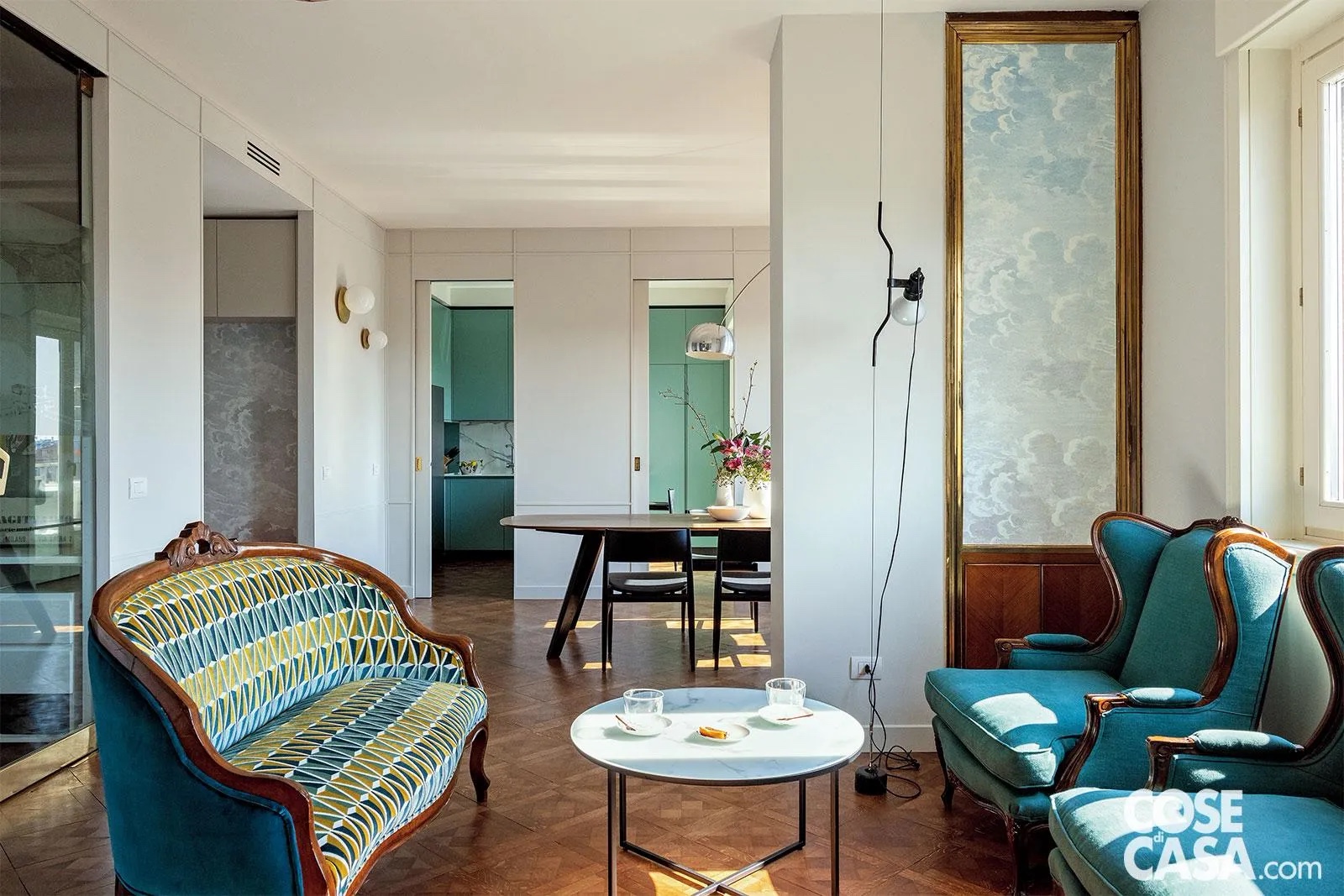 Nell’open space la zona conversazione al centro del volume ha un’impronta vintage: cornice dorata intorno alla nicchia, divanetto e poltrone in legno con rivestimenti in velluto. La lampada a sospensione è la Parentesi di Flos, design Achille Castiglioni e Pio Manzù. Sul tavolino rotondo, tazze da caffè di Villeroy & Boch. La nicchia è rivestita con carta da parati Nuvole al Tramonto di Cole & Son, design Piero Fornasetti. A sinistra, in fondo nella zona pranzo, applique Bijoux di Vesoi. Nell’open space la zona conversazione al centro del volume ha un’impronta vintage: cornice dorata intorno alla nicchia, divanetto e poltrone in legno con rivestimenti in velluto. La lampada a sospensione è la Parentesi di Flos, design Achille Castiglioni e Pio Manzù. Sul tavolino rotondo, tazze da caffè di Villeroy & Boch. La nicchia è rivestita con carta da parati Nuvole al Tramonto di Cole & Son, design Piero Fornasetti. A sinistra, in fondo nella zona pranzo, applique Bijoux di Vesoi.