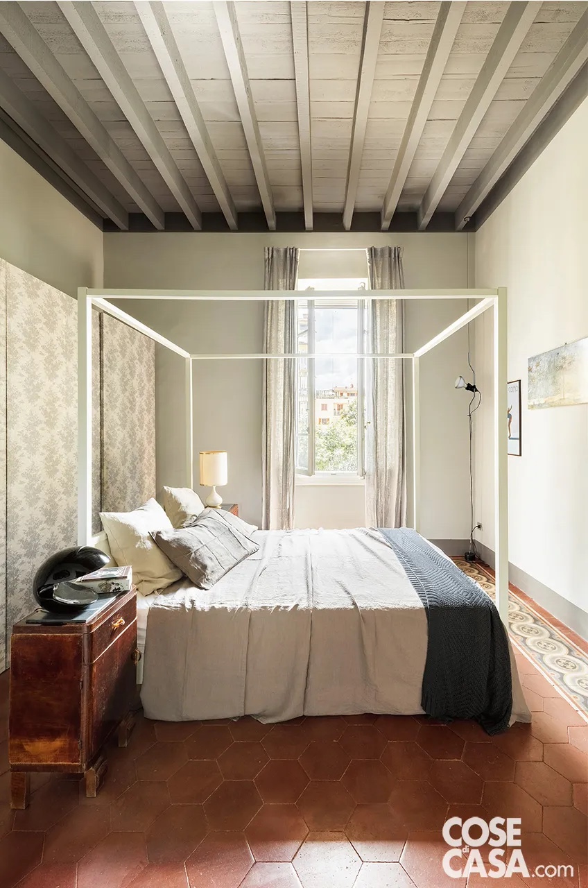 Nella camera matrimoniale, accanto al letto a baldacchino a centro stanza, una versione contemporanea di Maisons du Monde, il comodino è vintage anni ’40. L’abat-jour è un pezzo di famiglia, quella nera dall’altra parte è il modello Miss Pack di Tacchini. L’armadio ad ante scorrevoli, reinterpretato con la carta da parati è di Ikea. Il pavimento è originale in cementine, lo zoccolino è dipinto con smalto di Farrow & Ball. Nell’angolo vicino alla finestra, la lampada a sospensione è il modello Parentesi di Flos, design Achille Castiglioni e Pio Manzu. Nella camera matrimoniale, accanto al letto a baldacchino a centro stanza, una versione contemporanea di Maisons du Monde, il comodino è vintage anni ’40. L’abat-jour è un pezzo di famiglia, quella nera dall’altra parte è il modello Miss Pack di Tacchini. L’armadio ad ante scorrevoli, reinterpretato con la carta da parati è di Ikea. Il pavimento è originale in cementine, lo zoccolino è dipinto con smalto di Farrow & Ball. Nell’angolo vicino alla finestra, la lampada a sospensione è il modello Parentesi di Flos, design Achille Castiglioni e Pio Manzu.