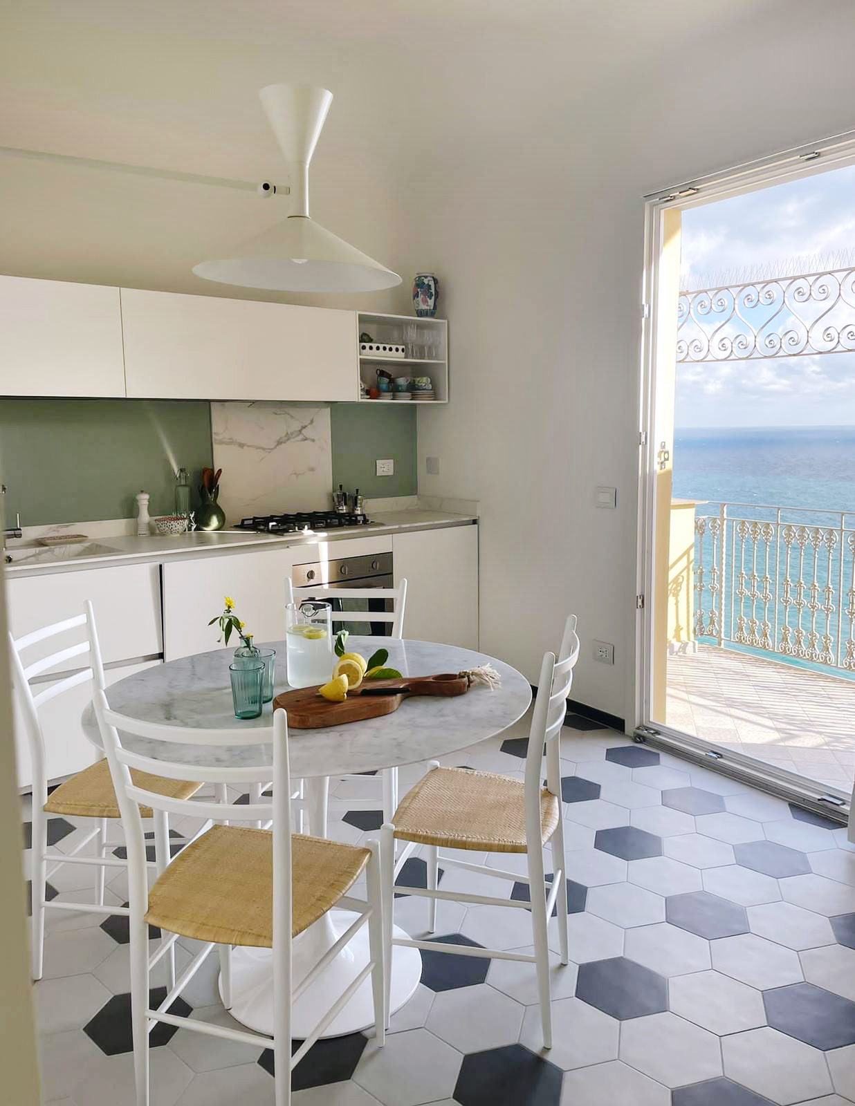 Cucina dopo la ristrutturazione, al mare, chiara con cementine bianco e nere a pavimento e tavolo rotondo bianco affacciata su balcone Cucina dopo la ristrutturazione, al mare, chiara con cementine bianco e nere a pavimento e tavolo rotondo bianco affacciata su balcone