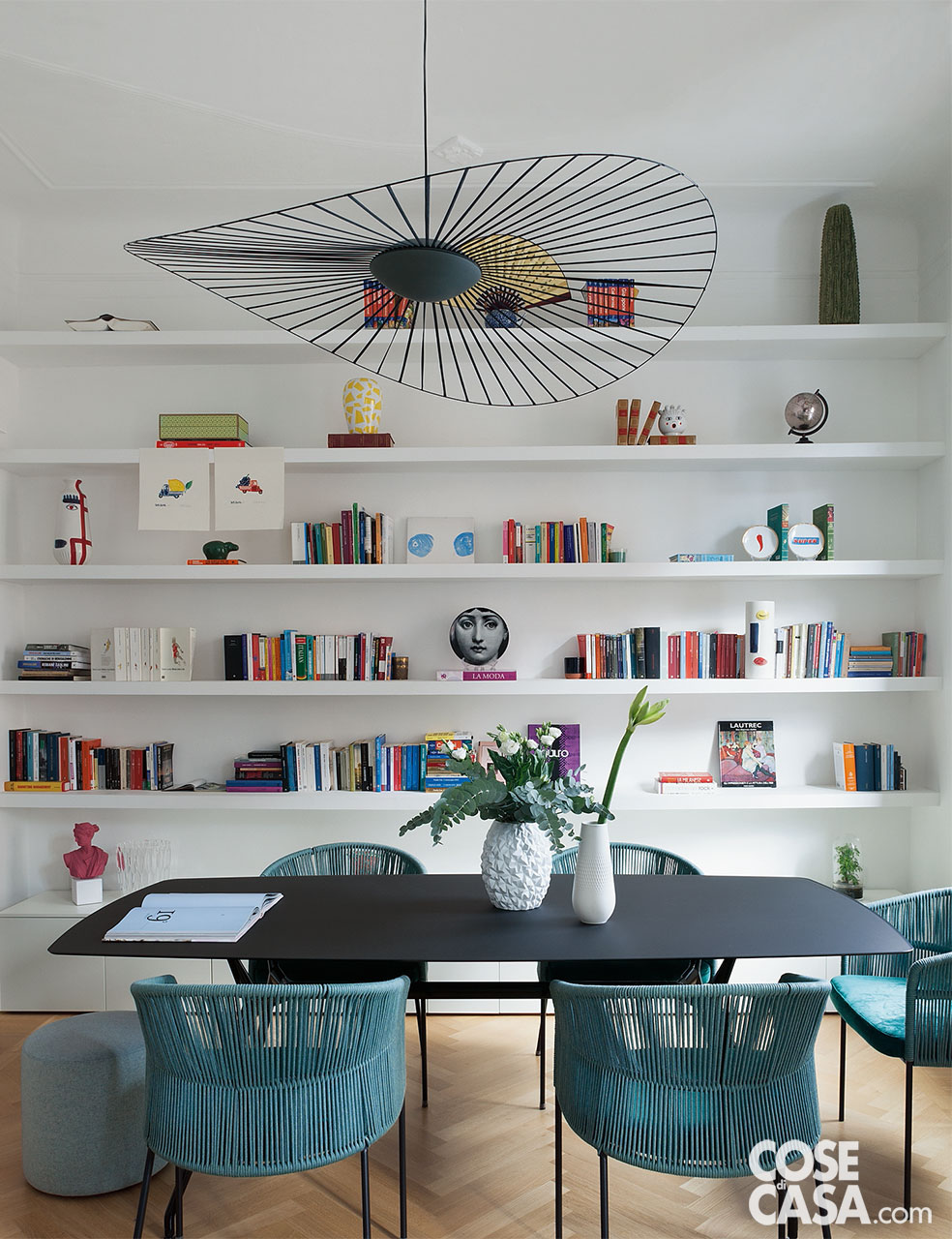 Zona pranzo con sedie azzurre e libreria a tutta parete come sfondo