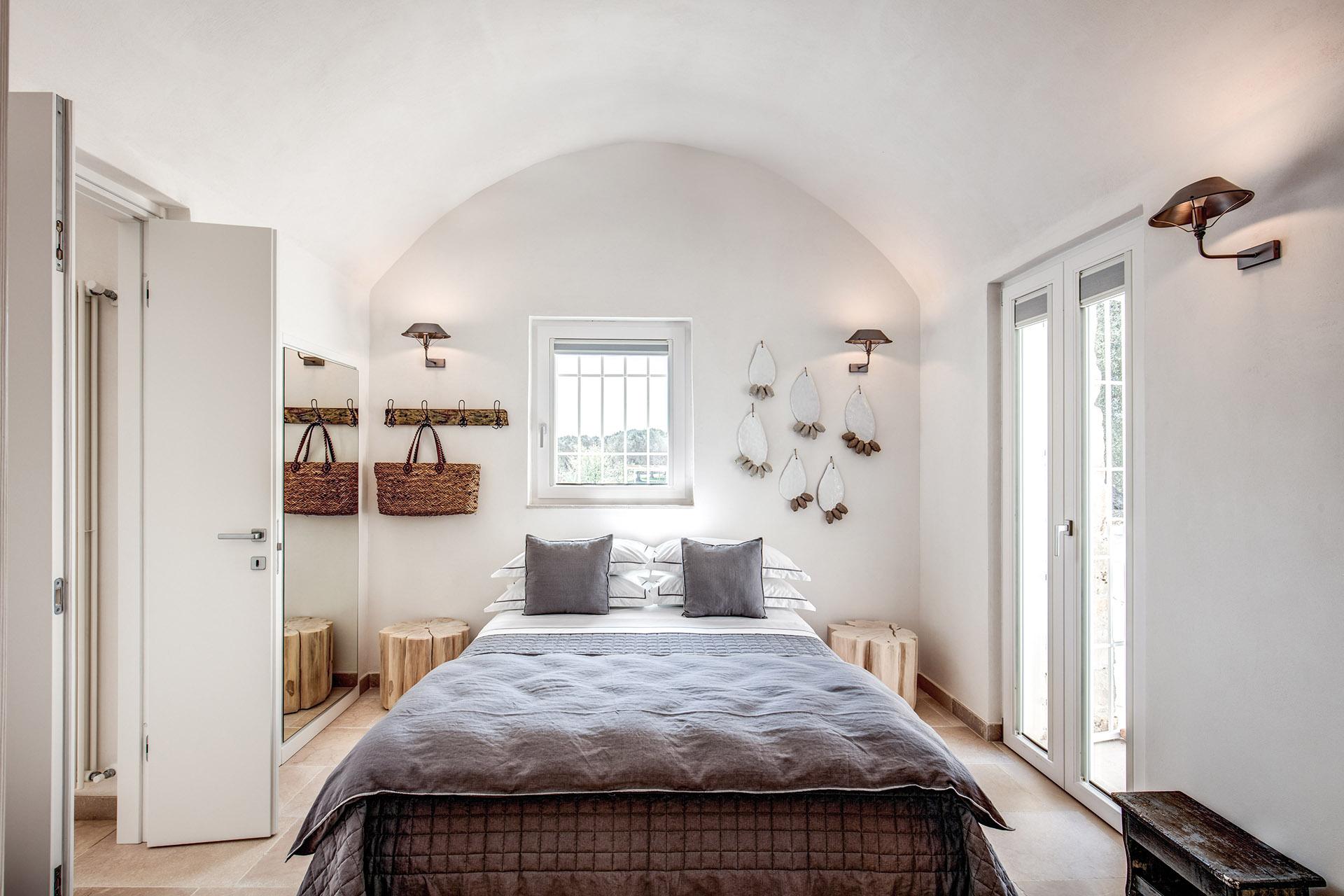 Nella camera essenziale e dalle dimensioni contenute, c’è tutto il necessario per una stanza sobria ma comoda: il letto e arredi naturali, come l’appendiabiti, i comodini, la panchetta, e gli elementi decorativi sulla parete - Progetto d’interni ed arredamento: Gian Paolo Guerra – Studio Guerra Interior Design & Home Shopping.