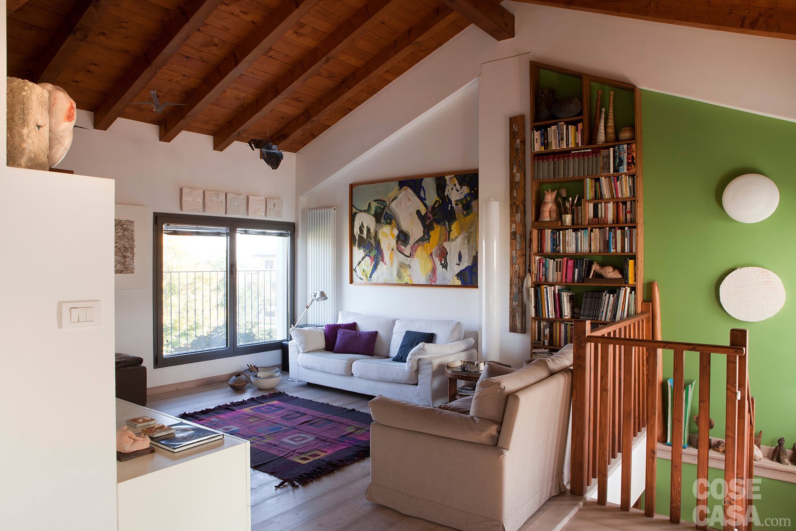 L’ingresso dell’appartamento è direttamente sul salotto, al quale si accede da una scala della ex cascina ristrutturata. La zona relax è circoscritta e abbellita da quadri che definiscono lo spazio delle pareti, a cui fanno da contorno le travi in legno. Anche la scelta di colori, dal verde dei tessili al verde sulla parete ridefiniscono l’ambiente di una struttura anticamente rustica - Foto: Cristina Galliena e Guelfa Rugarli. Progetto: geometra Mario Paronetto.