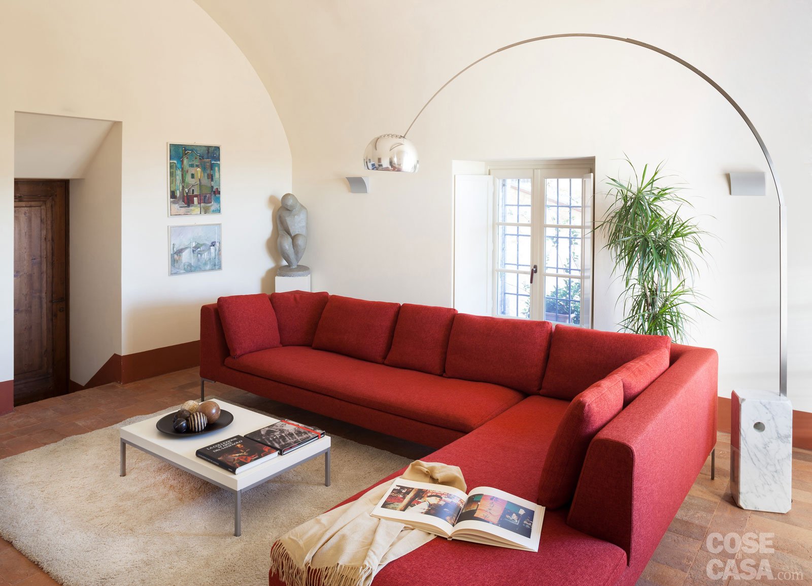 Il divano rosso protagonista di un salotto di campagna salotto. Un’area che invita al relax in una casa di base rustica ma con elementi moderni, come l’iconica lampada Arco di Flos e il tavolino basso al centro del tappeto chiaro - Foto: Cristina Fiorentini. Progetto: arch. Federico Lissignoli e interior designer Giulia Sbalchiero Studio 23architetture.