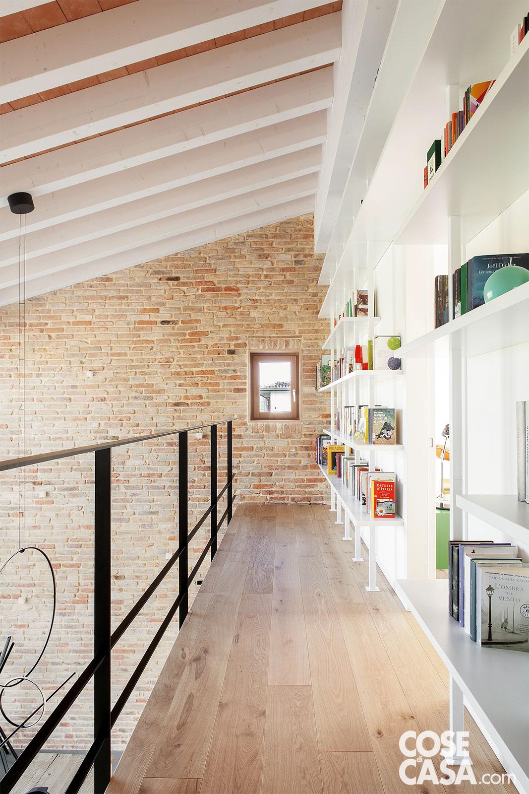 La villa di campagna moderna sfrutta l’altezza. Il soppalco è occupato da una libreria bianca, in continuità con le travi sbiancate, a cui fanno eco le tavelle in cotto e il parquet del pavimento. - Foto: Makethatstudio. Progetto: Tixa – Studio Associato di Ingegneria e Architettura (arch. Marco Alessi e ing. Federico Dalla Valle). Collaboratore: arch. Michela Carlesso.