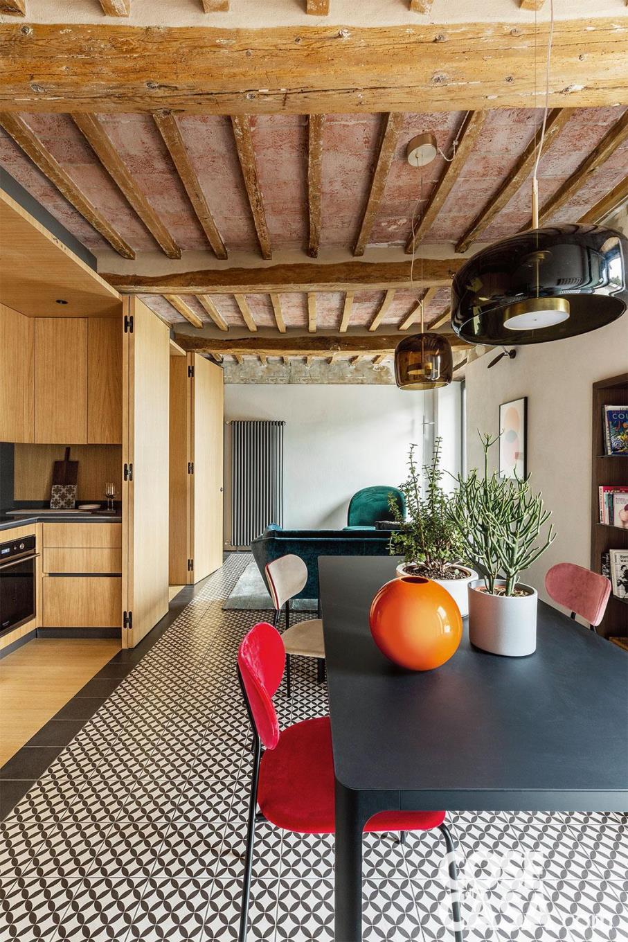 Un’affascinante abitazione dallo stile retrò, con sala da pranzo integrata nella cucina in legno. Tra sedie dai colori differenti e vaso arancione spiccano le due lampade a sospensione in vetro soffiato, due diverse versioni del modello Jube di Vistosi, che esaltano il clima naturale dell’ambiente – Foto: Studio Daido. Progetto: studio di architettura Massimo Zanelli.