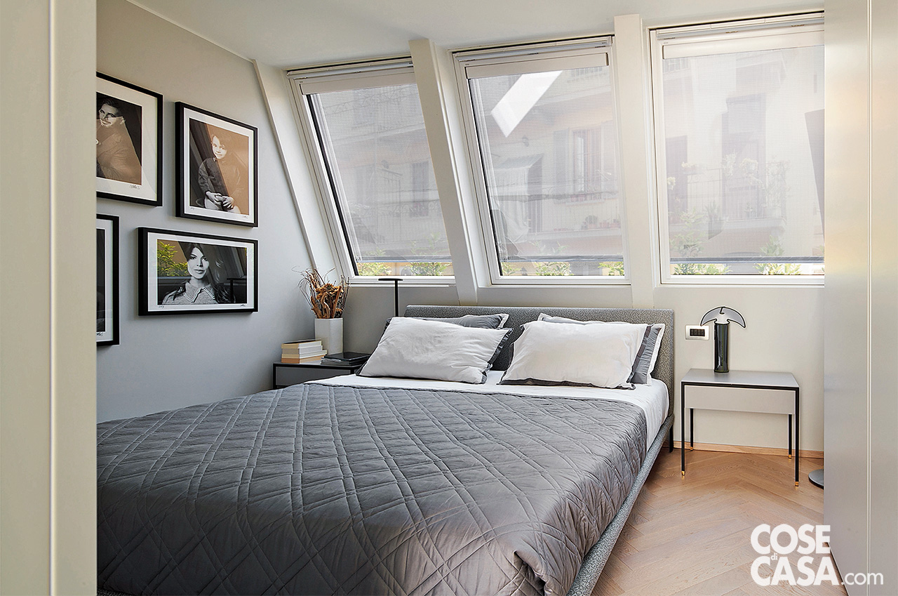 Camera matrimoniale con letto imbottito grigio posizionato sotto le finestre da tetto Camera matrimoniale con letto imbottito grigio posizionato sotto le finestre da tetto