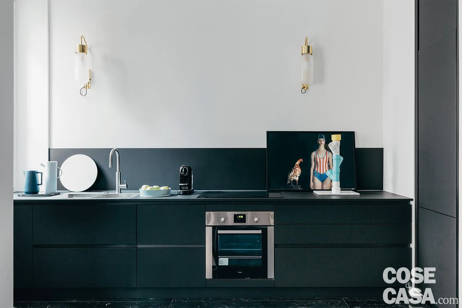 In un ambiente minimale con parete bianca e applique spicca una cucina senza pensili con cassettoni scorrevoli, elementi in acciaio e un’alzatina dello stesso colore delle ante e del piano, in continuità – Foto: Studio Roy. Styling: Chiara Dal Canto. Progetto: arch. Alessia Pessano e Chiara Novello, Studio A/C. In un ambiente minimale con parete bianca e applique spicca una cucina senza pensili con cassettoni scorrevoli, elementi in acciaio e un’alzatina dello stesso colore delle ante e del piano, in continuità – Foto: Studio Roy. Styling: Chiara Dal Canto. Progetto: arch. Alessia Pessano e Chiara Novello, Studio A/C.