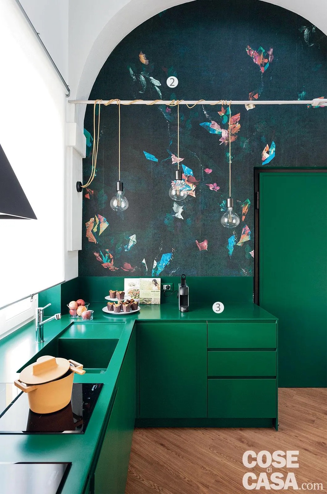 Nella stessa tonalità di verde dei mobili in laccato, i piani di lavoro sono in un materiale sintetico brevettato, il Pral®: è composto da elementi minerali mescolati a un polimero acrilico. Nell’angolo cottura, la carta da parti in vinilico che riveste la parete sotto l’arco è il modello Rafale di Wall & Decò. Le sospensioni, con il cavo avvolto intorno all’asta in metallo, che completano il bell'effetto della carta a parete sono il modello Sola di Renzo Serafini. Foto: Studio Roy. Styling: Rosaria Galli. Progetto: Bernuzzi Samori Architetti.