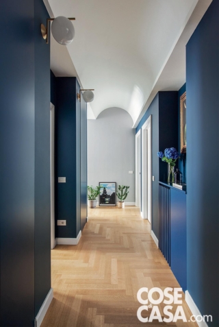 Il blu navy è stato scelto per tinteggiare le pareti del corridoio con soffitto a contrasto e parquet in legno chiaro. Dalla nicchia si nota un quadro con cornice oro che conferisce preziosità a questa area elegante e di grande impatto.